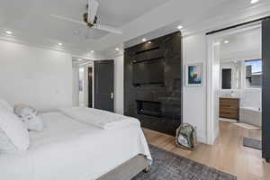 Bedroom with ornamental molding, ceiling fan, a fireplace, connected bathroom, and light hardwood / wood-style floors