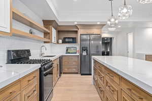 Kitchen with sink, stainless steel fridge, light stone countertops, decorative light fixtures, and gas stove