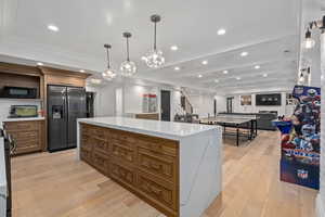 Kitchen featuring light stone countertops, stainless steel fridge, a spacious island, decorative light fixtures, and light hardwood / wood-style floors