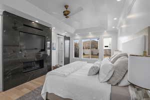 Bedroom featuring a tray ceiling, ceiling fan, dark wood-type flooring, a barn door, and a premium fireplace