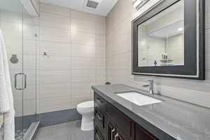 Bathroom with vanity, a shower with door, toilet, and tile walls