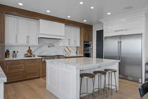 Kitchen featuring decorative backsplash, light stone countertops, stainless steel appliances, white cabinets, and a center island