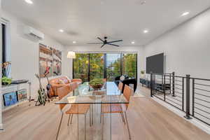 Dining room with a wall mounted AC, ceiling fan, and light wood-type flooring