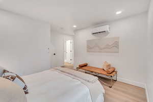 Bedroom with light wood-type flooring and a wall unit AC