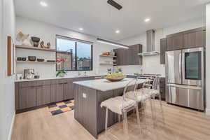 Kitchen with a center island, sink, wall chimney exhaust hood, hanging light fixtures, and stainless steel fridge