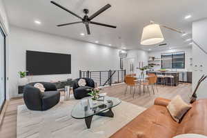 Living room featuring a wall mounted AC, light wood-type flooring, and ceiling fan