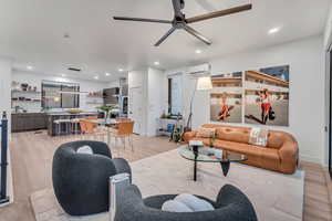 Living room with a wall mounted AC, ceiling fan, and light hardwood / wood-style flooring