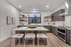 Kitchen featuring a kitchen breakfast bar, double oven range, wall chimney range hood, and backsplash