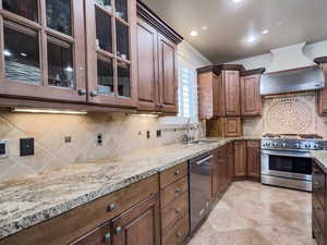 Kitchen featuring wall chimney exhaust hood, stainless steel appliances, sink, and light stone counters