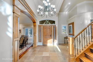 Entryway with a high ceiling, ornamental molding, light tile patterned floors, and an inviting chandelier