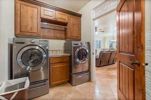 Washroom with ceiling fan with notable chandelier, cabinets, independent washer and dryer, and light tile patterned floors