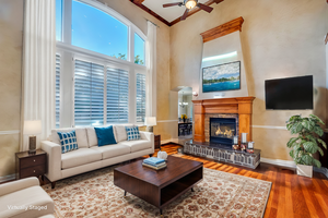 Living room with ceiling fan, hardwood / wood-style floors, a high ceiling, a fireplace, and ornamental molding