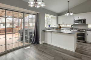 Kitchen with hanging light fixtures, an inviting chandelier, lofted ceiling, white cabinets, and appliances with stainless steel finishes