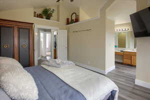 Bedroom with ensuite bath, ceiling fan, sink, vaulted ceiling, and light wood-type flooring