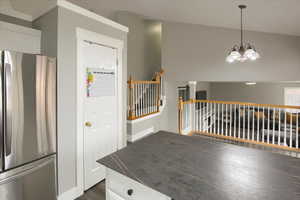 Kitchen with white cabinets, hanging light fixtures, vaulted ceiling, stainless steel fridge, and a notable chandelier