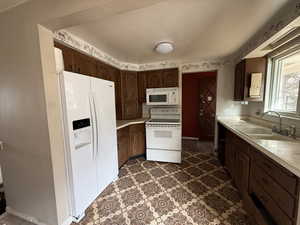 Kitchen with white appliances, dark brown cabinetry, and sink