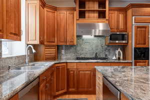 Kitchen featuring sink, stainless steel appliances, wall chimney range hood, tasteful backsplash, and stone countertops