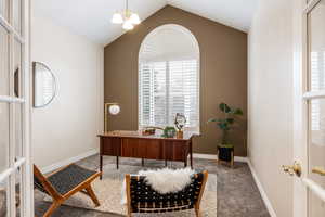 Office area featuring carpet, vaulted ceiling, and a notable chandelier