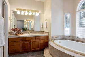 Bathroom featuring vanity, a relaxing tiled tub, and plenty of natural light