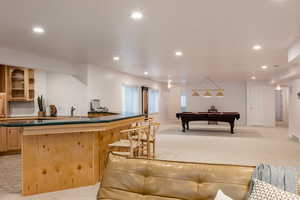 Bar with light brown cabinets, light colored carpet, sink, and pool table