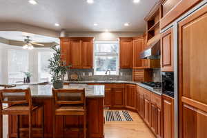 Kitchen with a breakfast bar, ventilation hood, sink, a kitchen island, and light stone counters