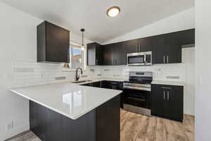 Kitchen featuring lofted ceiling, sink, decorative light fixtures, appliances with stainless steel finishes, and kitchen peninsula