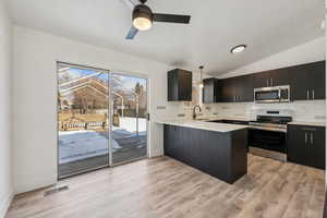 Kitchen featuring kitchen peninsula, vaulted ceiling, hanging light fixtures, appliances with stainless steel finishes, and sink