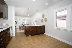 Kitchen featuring pendant lighting, dark brown cabinets, backsplash, and light hardwood / wood-style flooring