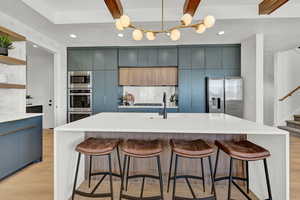 Kitchen with a kitchen island with sink, light wood-type flooring, beam ceiling, a kitchen bar, and stainless steel appliances