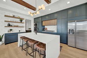 Kitchen with appliances with stainless steel finishes, sink, blue cabinetry, a center island with sink, and beamed ceiling