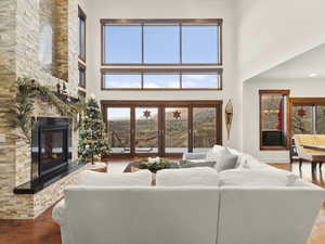 Living room featuring hardwood / wood-style floors, a towering ceiling, and a stone fireplace