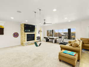 Living room featuring a stone fireplace, ceiling fan, light carpet, and ornamental molding