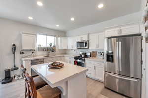 Kitchen featuring a center island, a kitchen breakfast bar, sink, appliances with stainless steel finishes, and white cabinetry