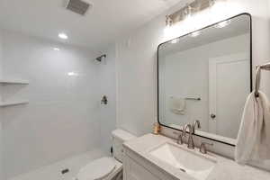 Bathroom featuring tiled shower, vanity, and toilet