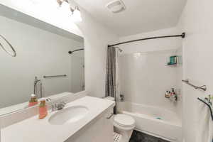 Full bathroom with shower / bath combo, vanity, a textured ceiling, and toilet