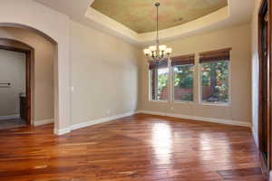 Empty room with a tray ceiling, an inviting chandelier, and hardwood / wood-style flooring