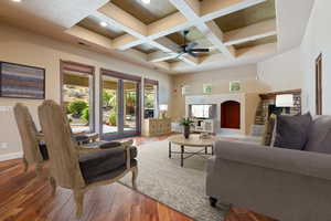 Living room featuring coffered ceiling, ceiling fan, beam ceiling, wood-type flooring, and a stone fireplace