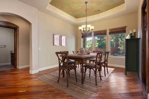 Dining room with a notable chandelier, dark hardwood / wood-style flooring, and a raised ceiling