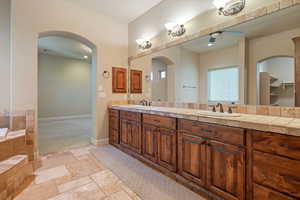 Bathroom with a relaxing tiled tub, vanity, and ceiling fan