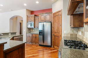 Kitchen with decorative backsplash, light stone counters, light wood-type flooring, and appliances with stainless steel finishes