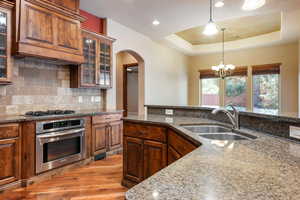 Kitchen featuring sink, stainless steel appliances, a raised ceiling, a chandelier, and dark stone counters