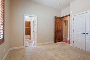 Unfurnished bedroom featuring ensuite bathroom, a closet, and light colored carpet