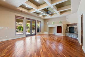 Unfurnished living room with coffered ceiling, ceiling fan, a fireplace, beam ceiling, and wood-type flooring