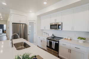 Pics are of model home.Kitchen featuring tasteful backsplash, white cabinetry, sink, and stainless steel appliances