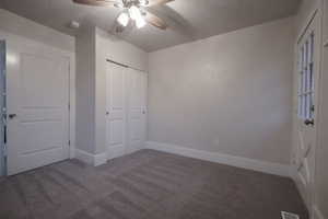 Unfurnished bedroom featuring ceiling fan, a closet, a textured ceiling, and dark colored carpet