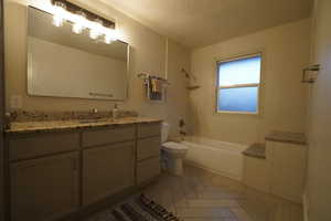 Full bathroom featuring toilet, vanity, a textured ceiling, and tiled shower / bath