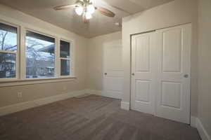 Unfurnished bedroom featuring dark colored carpet, a closet, and ceiling fan