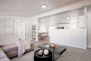 Carpeted living room featuring vaulted ceiling with beams and a textured ceiling