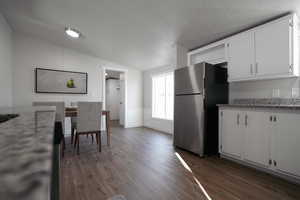 Kitchen featuring white cabinets, dark wood-type flooring, stainless steel refrigerator, and vaulted ceiling