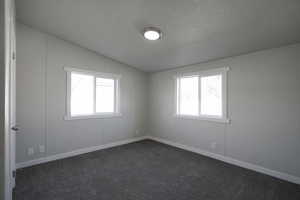 Spare room featuring a textured ceiling, dark carpet, and vaulted ceiling